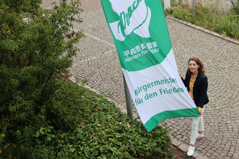 Eine Frau h&auml;lt die Mayors-for-Peace-Flagge bevor sie gehisst wird.